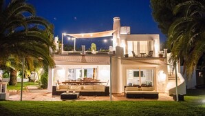 A modern two-story house with a patio area, outdoor furniture, and a large window overlooking the garden. - Villa, 8BR, Sea views, walk to the beach, pool house (Ibiza)