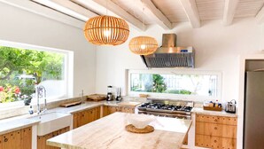 A modern kitchen with wooden cabinets, a central island, a gas stove, and pendant lighting. - Villa, 8BR, Sea views, walk to the beach, pool house (Ibiza)