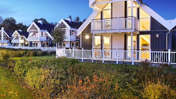 A row of modern, multi-story vacation homes with balconies, white railings, and a well-maintained garden in the foreground.