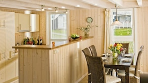 A kitchen with wooden cabinets, a central island with a sink, and a dining area with wicker chairs and a table set for two.
