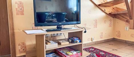 A television on a wooden stand with books and a remote control, a patterned rug, and a wooden ceiling structure.