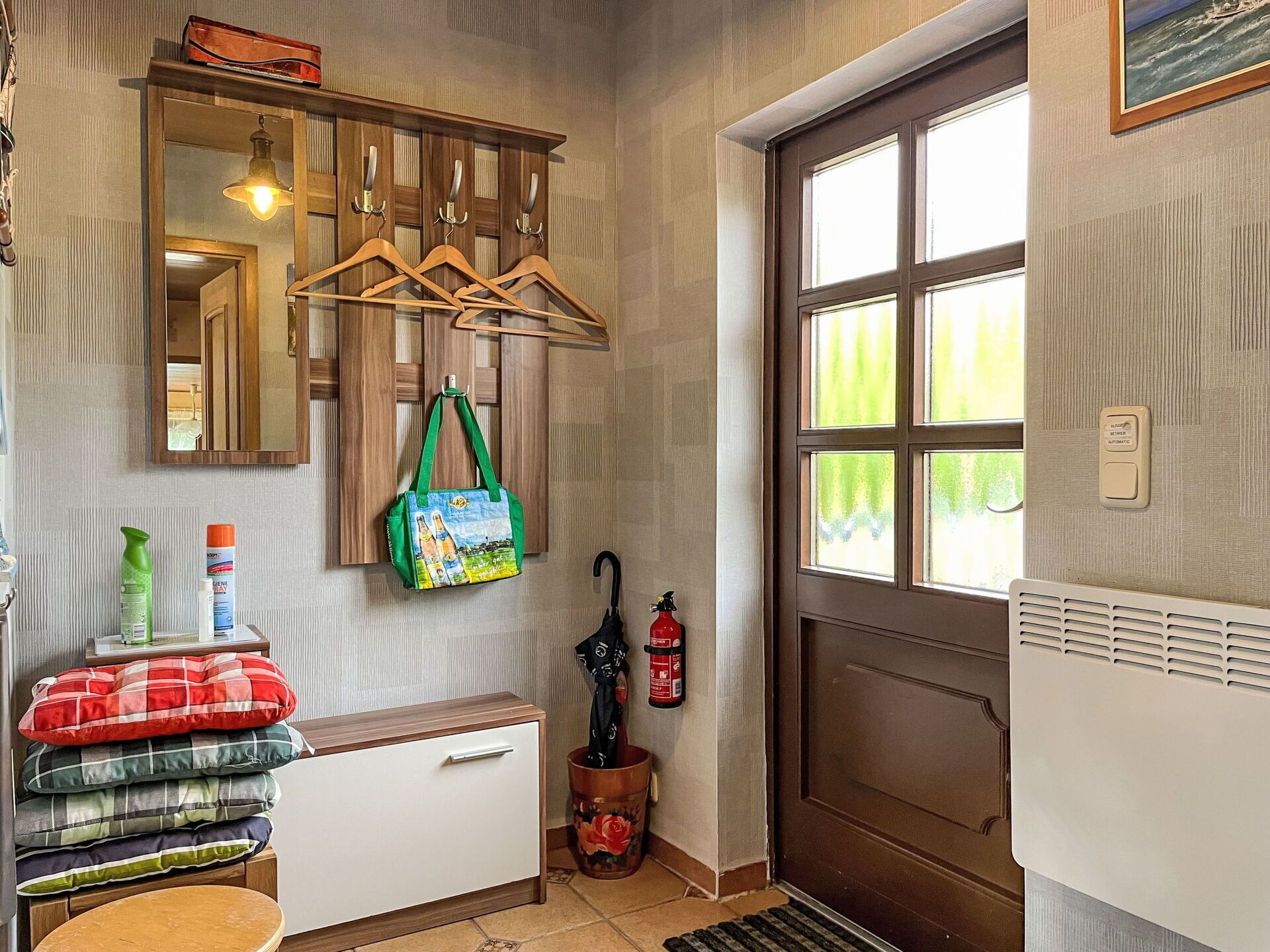 A hallway with a coat rack, a mirror, a fire extinguisher, and a door with a window.