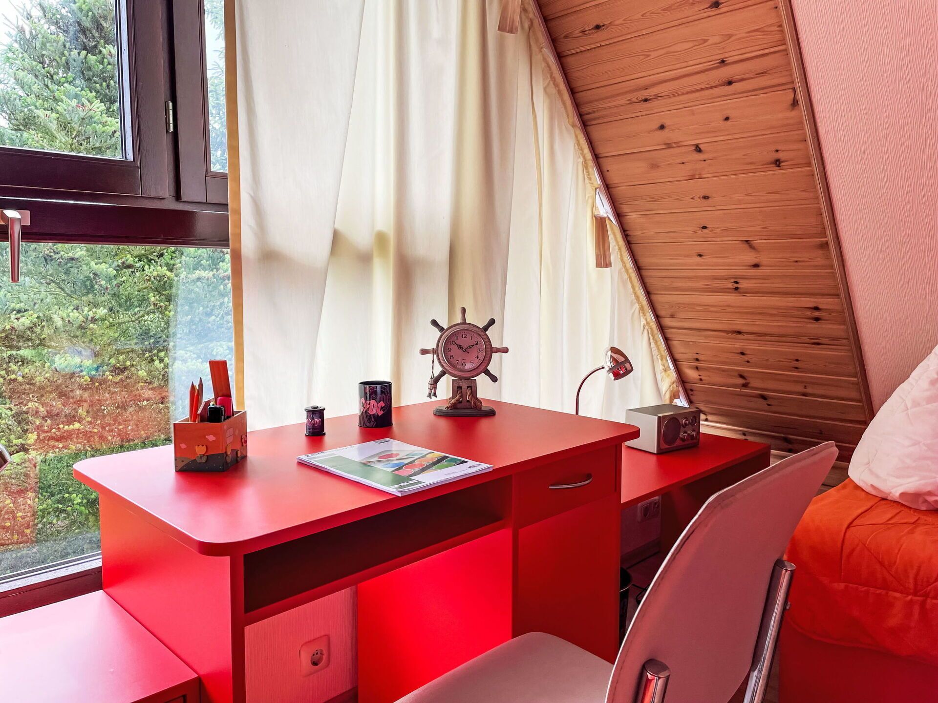 A red desk with a ship's wheel, a lamp, and a speaker in a tent-like room with a window and curtains.