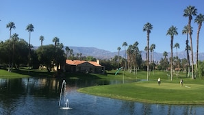 Ein Golfplatz mit Teich, Palmen und einem Gebäude mit rotem Dach.