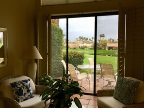 A room with a sliding glass door leading to an outdoor patio area with a table and chairs, a lamp, and a sofa with patterned cushions.