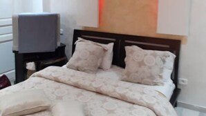 A bedroom with a bed, pillows, a TV on a stand, and a ceiling with red lighting. - The Chedy Home (Ariana)