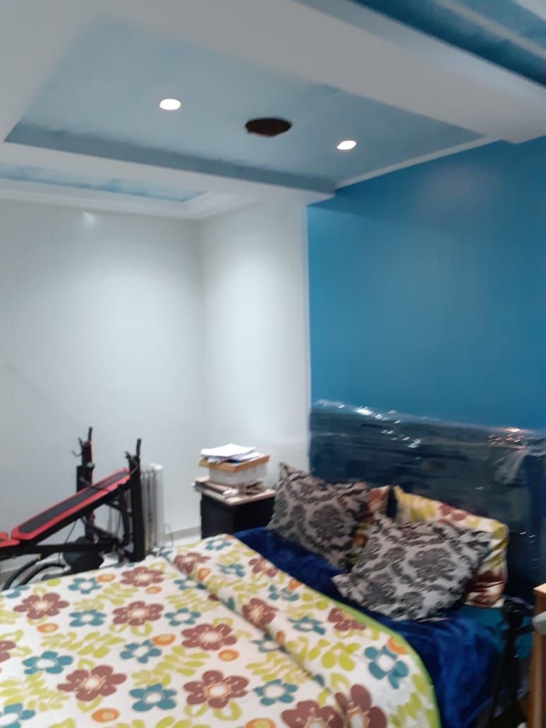 A bedroom with a bed, pillows, a radiator, and a desk with items on it.