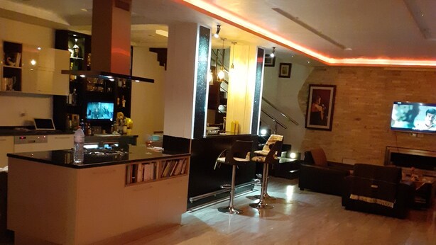 A modern kitchen with a bar area, a dining space with a sofa, and a TV mounted on the wall. - The Chedy Home (Ariana)