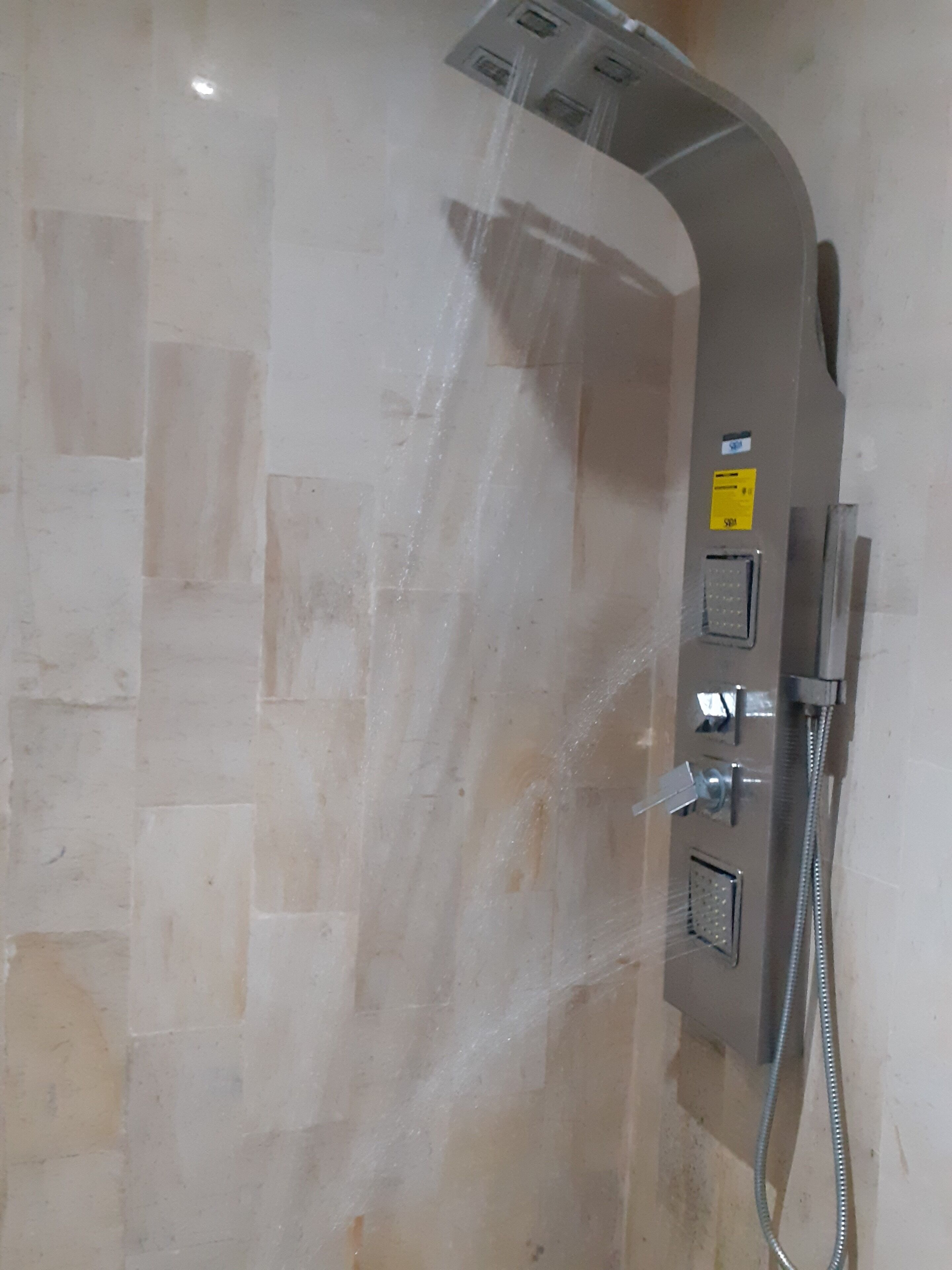 A shower with a curved design, a handheld showerhead, and a control panel with a yellow sticker.