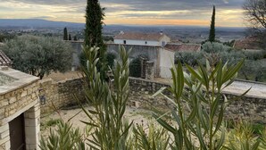 A stone building with a tiled roof, surrounded by olive trees and a view of a distant town. - les-pepites-de-Badou.fr present LA GRAVIERE -Classified 4 *- (Le Barroux)