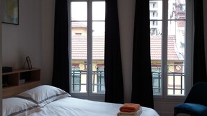 Hotellihuone, jossa on sänky, tuoli ja ikkuna, jossa on verhot.