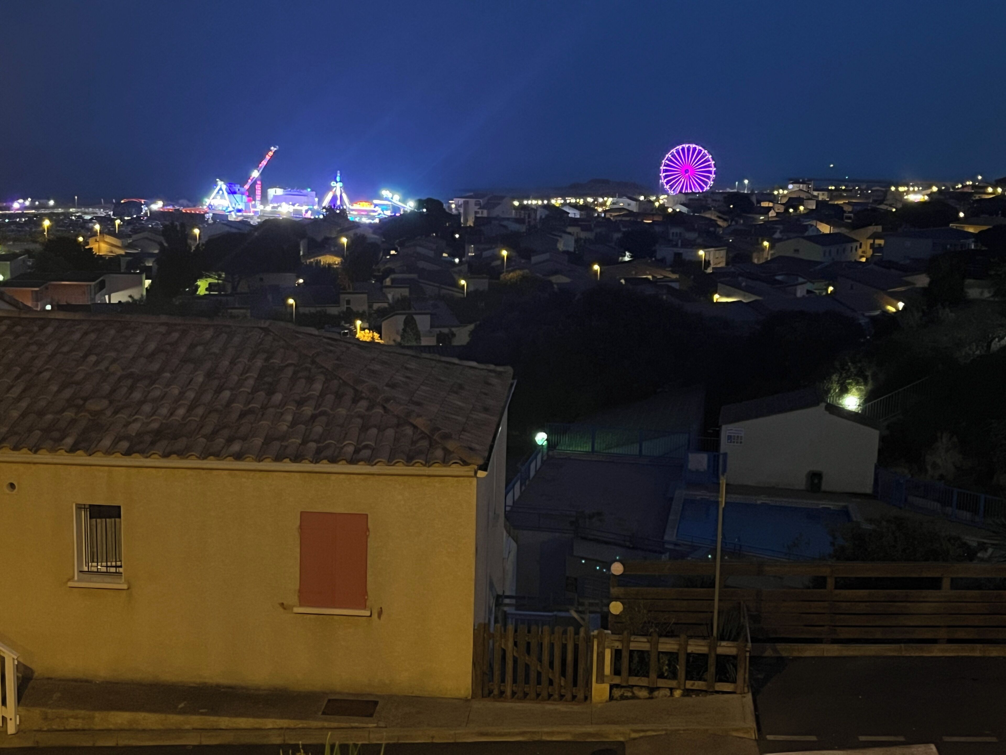 A residential area with a prominent Ferris wheel in the distance, surrounded by houses and streetlights.