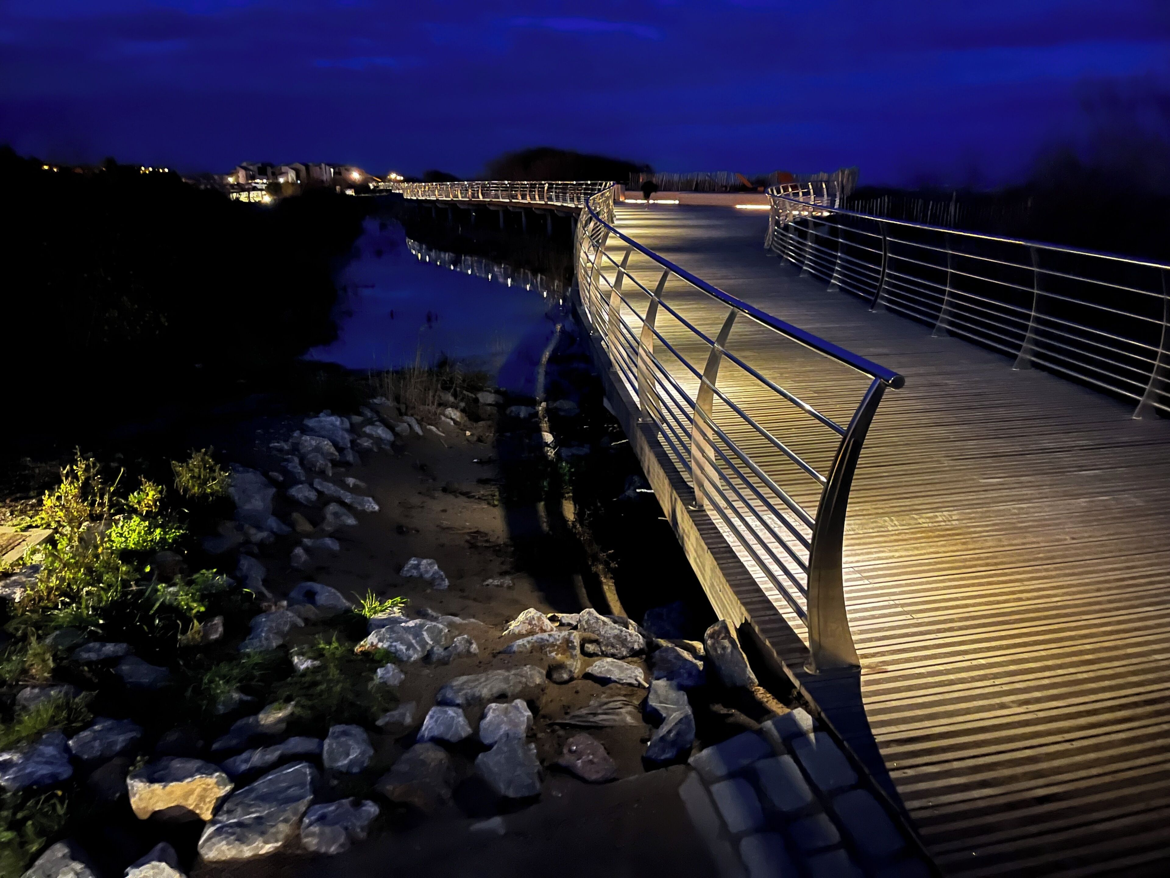 A nighttime view of a bridge with metal railings and a wooden walkway.