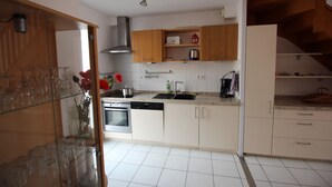 Een moderne keuken met witte kastjes, roestvrijstalen apparatuur en een glazen vitrine met wijnglazen.