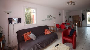 Een woonkamer met een bank, een eettafel met stoelen, een televisie en een lamp.