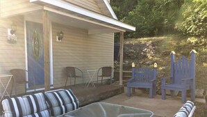 A covered patio with a glass table, striped sofa, and blue Adirondack chairs. - Hillside Cottage in Beautiful Downtown Hermann (Hermann)
