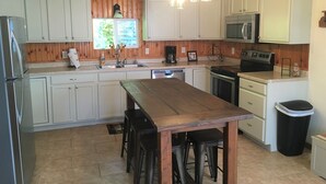 A kitchen with wooden paneling, white cabinets, a central island with stools, stainless steel appliances, and pendant lighting. - Hillside Cottage in Beautiful Downtown Hermann (Hermann)