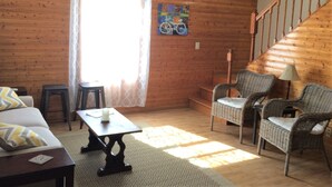 A cozy living room with a wooden floor, a staircase, wicker chairs, a sofa, a small table, and a window with curtains. - Hillside Cottage in Beautiful Downtown Hermann (Hermann)