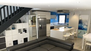 Een moderne keuken met een centraal eiland, een eetgedeelte met witte stoelen en een grijze modulaire bank.