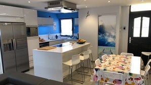 Een moderne keuken met een centraal eiland, witte stoelen en een eettafel met een tafelkleed met fruitprint.