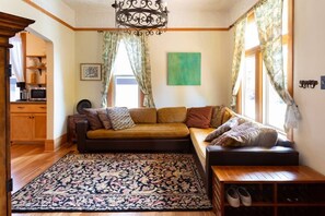 A cozy living room with a sofa, a coffee table, and a rug. There is a wooden cabinet and a window with curtains.