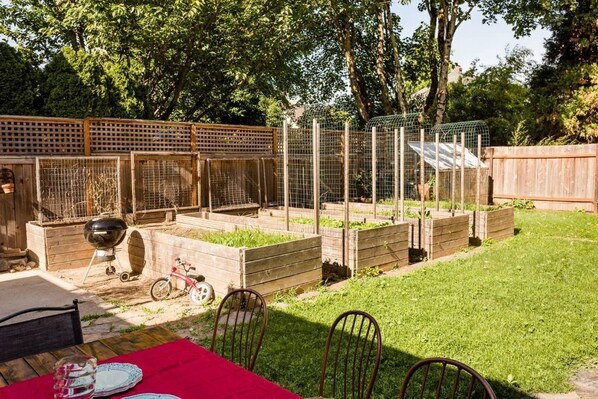 A backyard with raised garden beds, a grill, and a dining table with chairs.