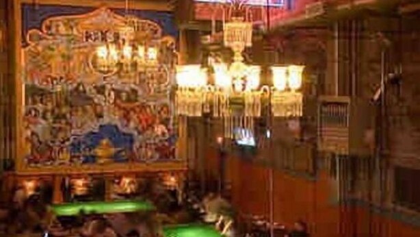 Een biljartzaal met meerdere tafels, een muurschildering en kroonluchters.
