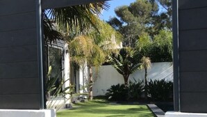 A staircase leading to a well-maintained garden with a lawn, palm trees, and a white wall.