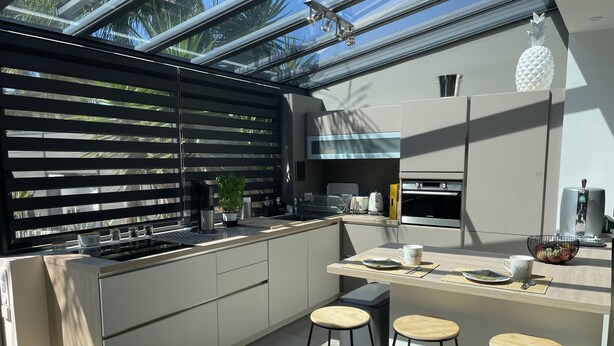 A modern kitchen with a large island, bar stools, a coffee machine, and a view through the window.