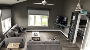 Ein modernes Wohnzimmer mit einem grauen Sofa, einem Holztisch und einem Deckenventilator.