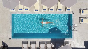 Vista aérea de una piscina con una persona nadando, rodeada de sillas de descanso y sombrillas.