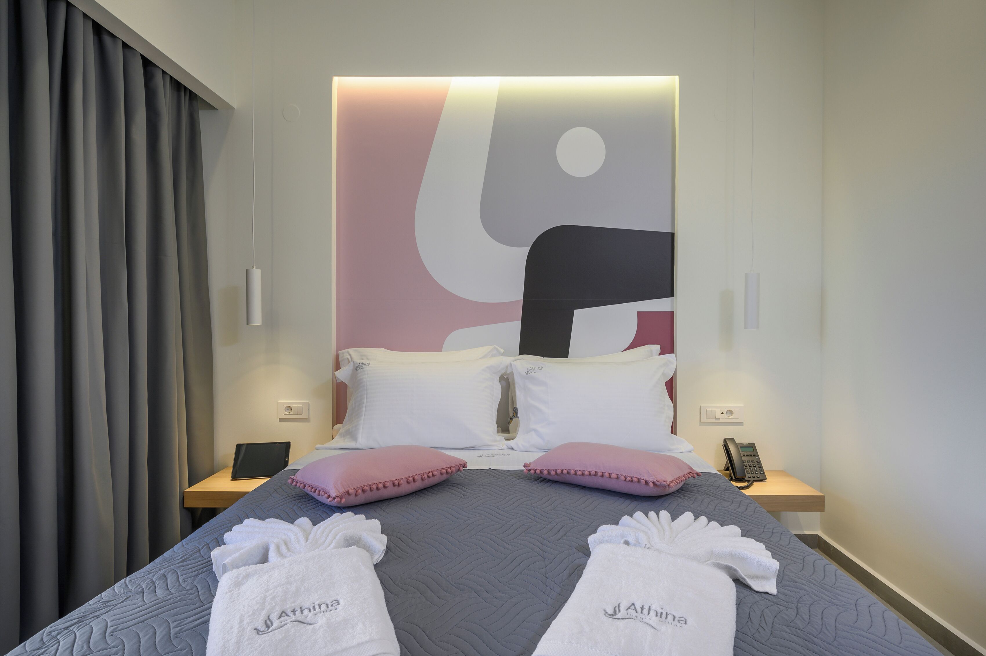 A hotel room with a bed, pillows, a bedside table with a phone, and a tablet.