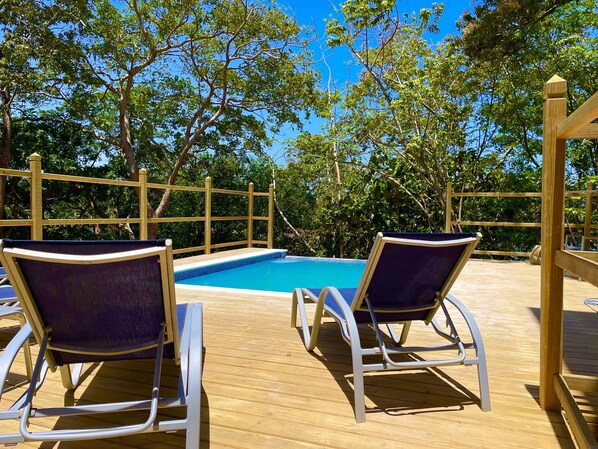 Een houten terras met twee ligstoelen en een zwembad.