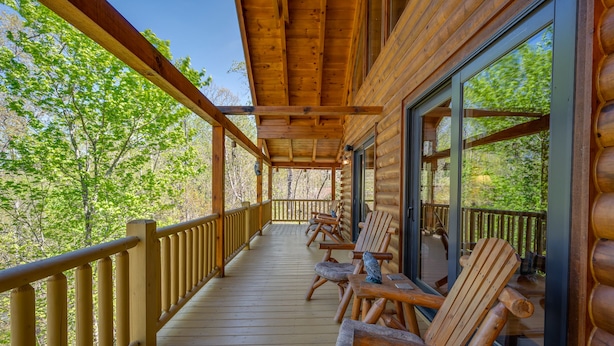 A wooden deck with log railing, wooden chairs, and a glass door leading to a forested area.
