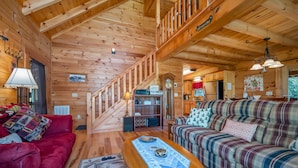 A wooden cabin interior with a red sofa, plaid sofa, and a wooden coffee table.