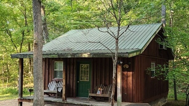 Eine rustikale Holzhütte mit Veranda, einer grünen Tür und einem kleinen Fenster.