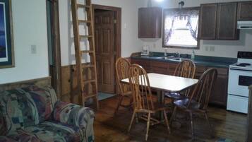 A cozy kitchen with wooden cabinets, a dining table with chairs, a ladder, and a ceiling fan.