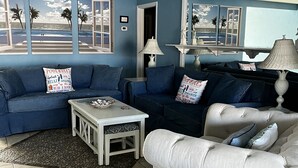 A living room with a blue wall, a ceiling fan, a white sofa, and a coffee table. - Heated pool, large home across from the beach. Lots of amenities included. (Ormond Beach)