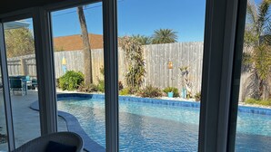 A view of a swimming pool from a covered patio area with wicker furniture and a table. - Heated pool, large home across from the beach. Lots of amenities included. (Ormond Beach)
