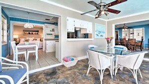 A spacious living area with a glass dining table, white wicker chairs, and a ceiling fan. - Heated pool, large home across from the beach. Lots of amenities included. (Ormond Beach)