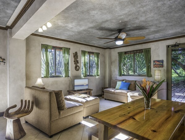 Un soggiorno con un tavolo da pranzo in legno, due divani, una TV e una ventola a soffitto.