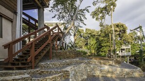 Una escalera de piedra conduce a una terraza de madera con vistas a un edificio y árboles.