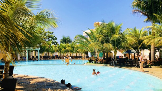 A swimming pool area with lounge chairs, palm trees, and a covered seating area. - Lacqua di Roma Hotel with Water Park and Flats complete with Kitchen (Caldas Novas)