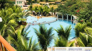 A large swimming pool surrounded by lush greenery and palm trees, with a building in the background. - Lacqua di Roma Hotel with Water Park and Flats complete with Kitchen (Caldas Novas)