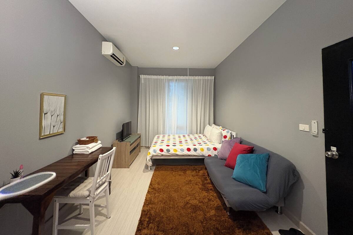 A compact bedroom with a bed, a sofa, a desk, and a chair.