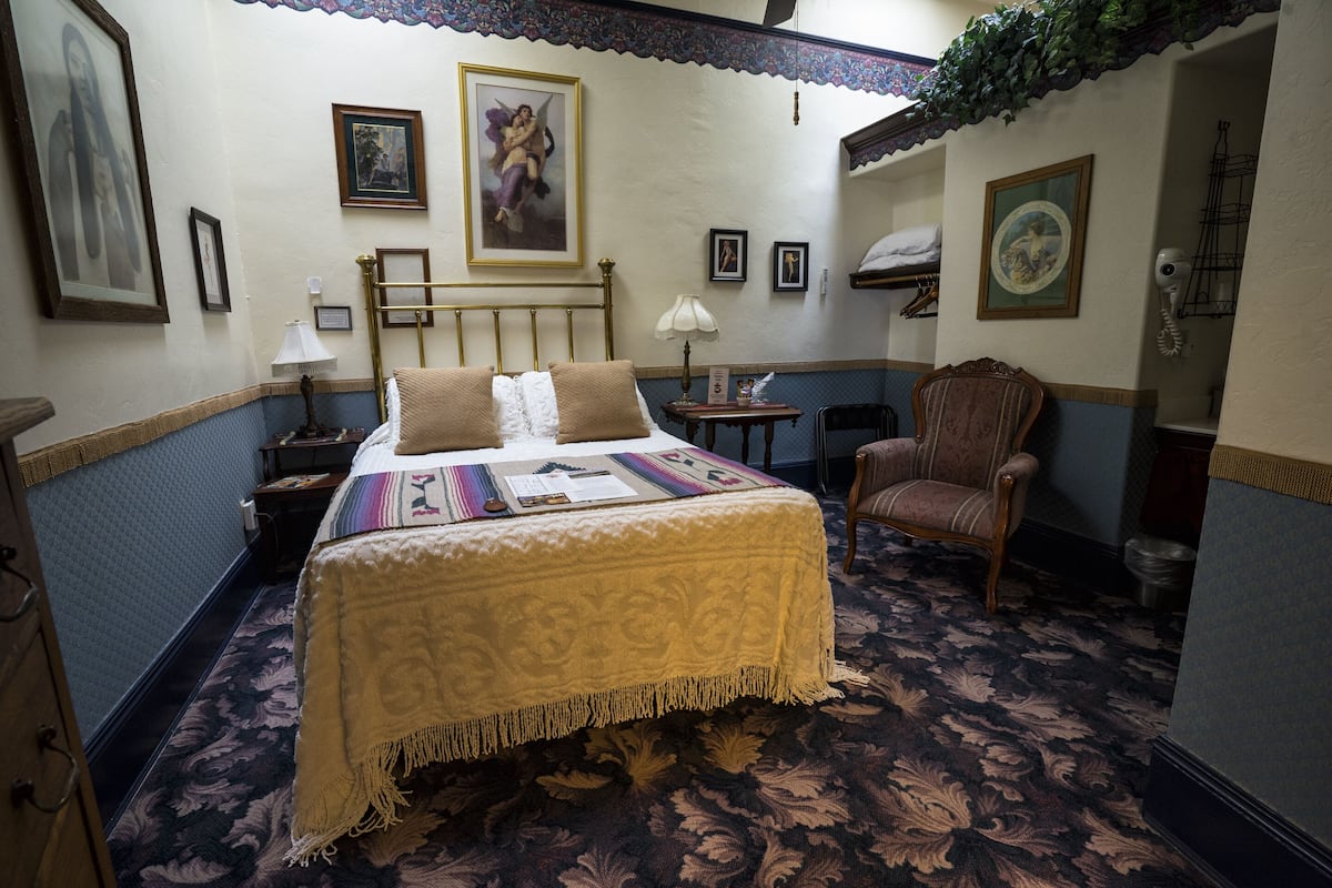 Une chambre d’hôtel avec un lit, une chaise, une petite table et un mur orné de tableaux.