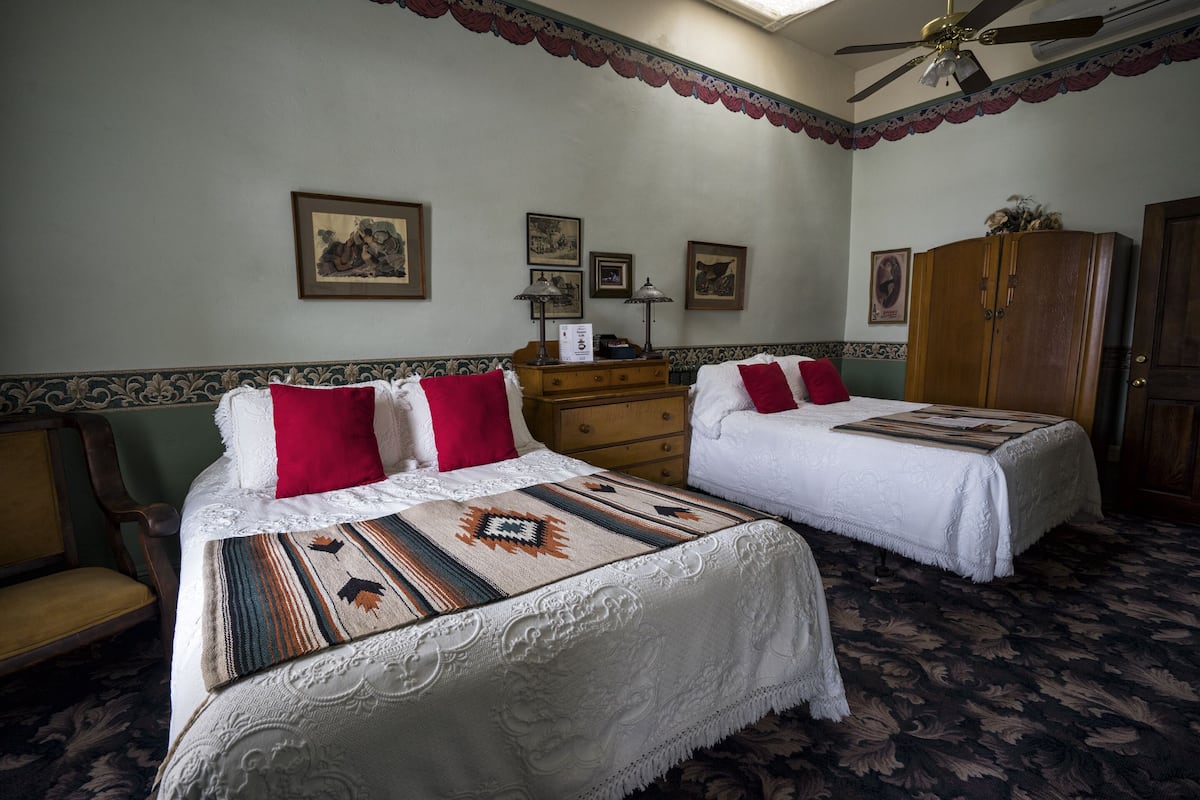 Une chambre d’hôtel avec deux lits, une armoire en bois et un ventilateur de plafond.