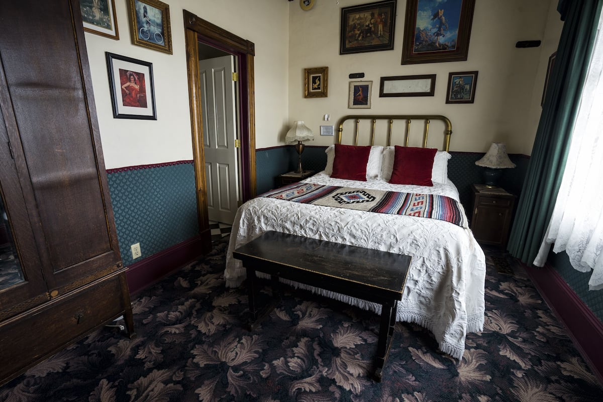 Une chambre à coucher avec un lit, un banc, une commode et une porte.