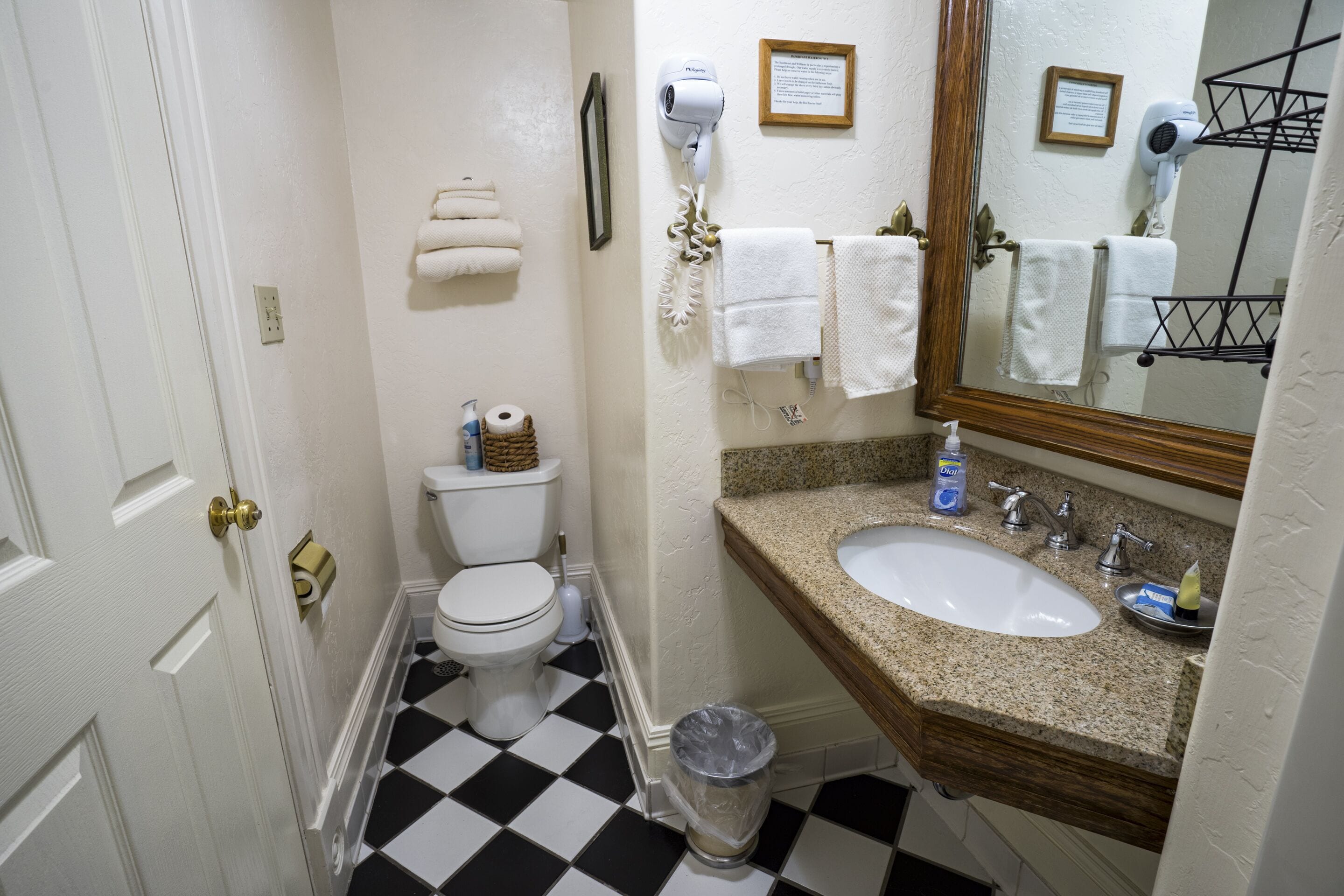 Un baño con inodoro blanco, lavamanos con encimera de granito y espejo con marco de madera.