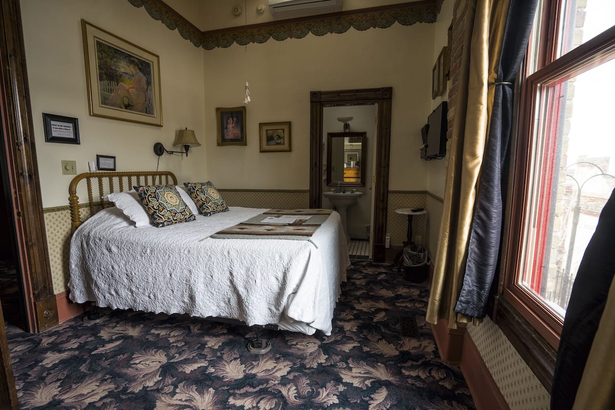 Une chambre à coucher avec un grand lit, une table de chevet, un miroir et une fenêtre avec des rideaux.